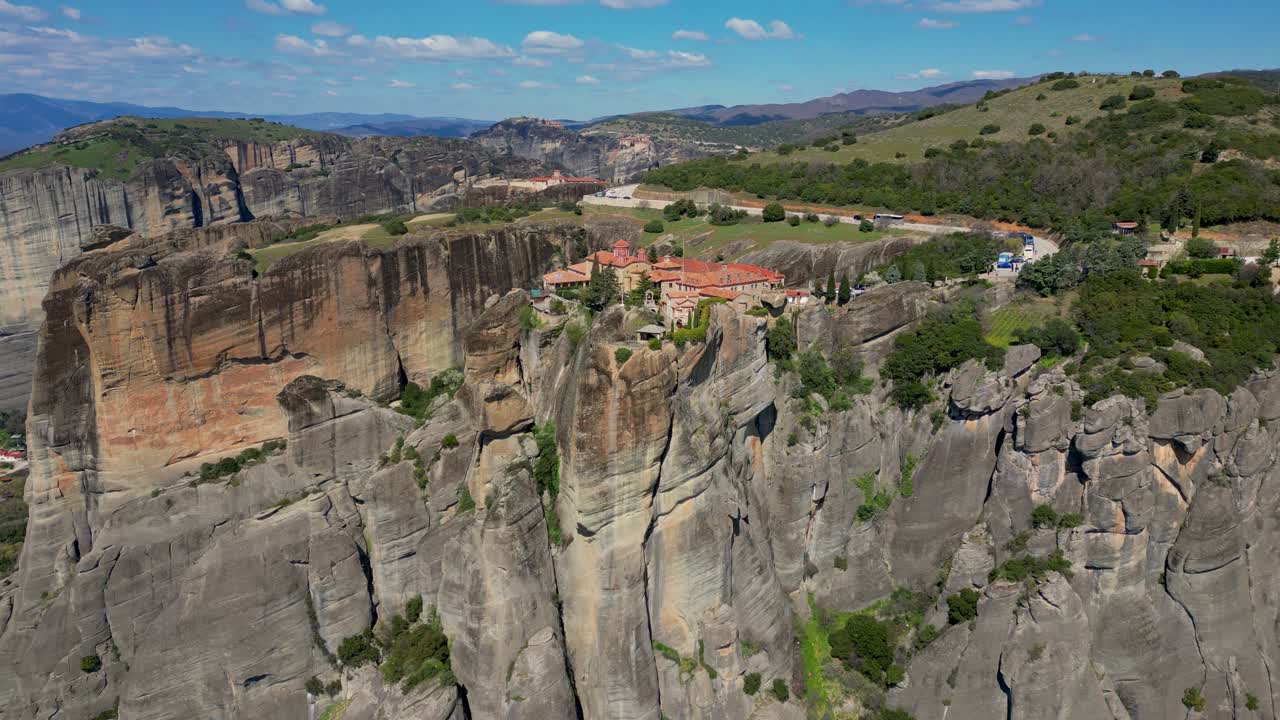 Wide aerial reveal of Roussanou Monastery atop towering cliff in dramatic Greek valley