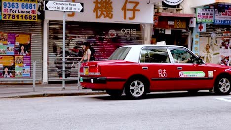 a red taxi drives past a busy street