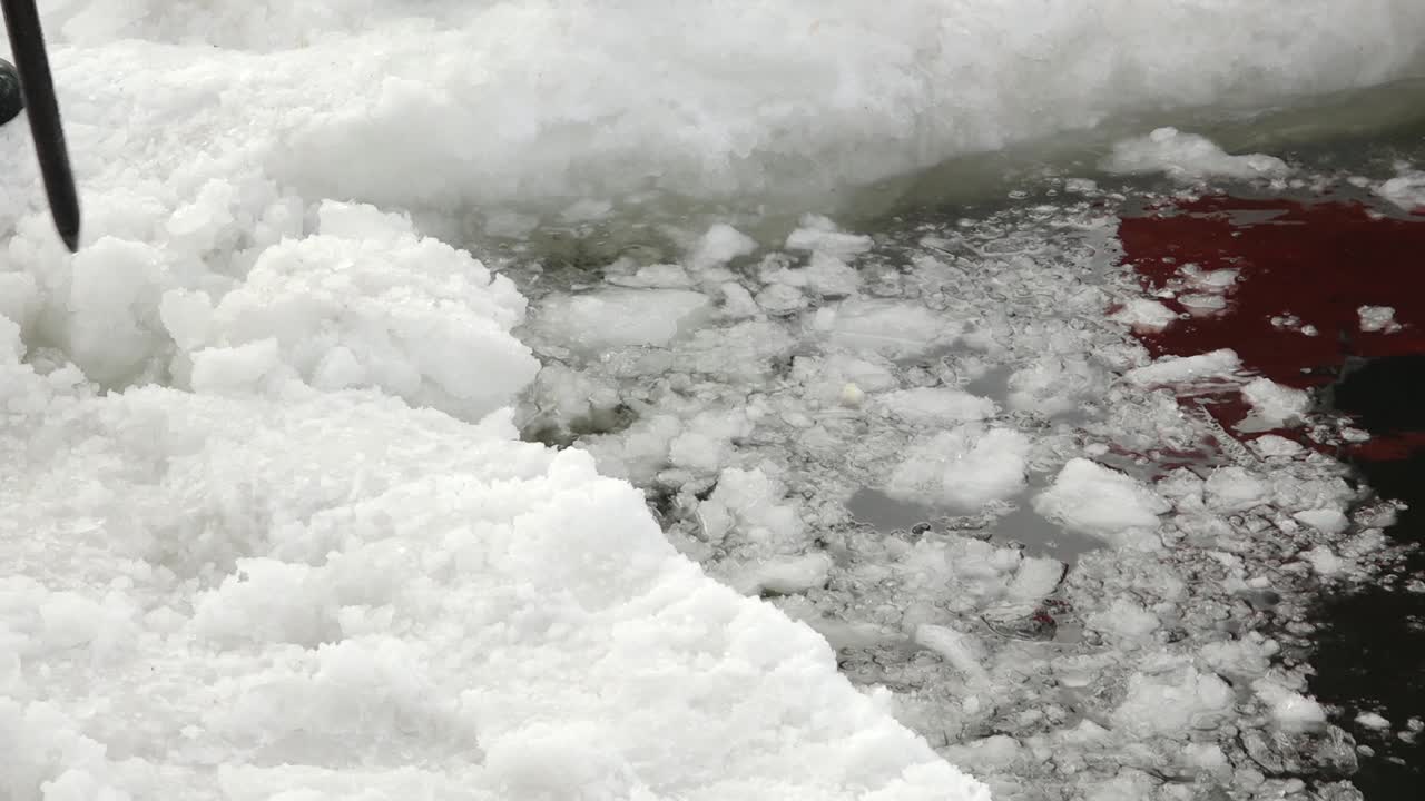 Nahaufnahme von Werkzeugen, die Eis von einem zugefrorenen See brechen und entfernen, um ein Eisloch unter winterlichen Bedingungen zu schaffen, mit schwimmenden Eisbrocken und kalter Wassertextur
