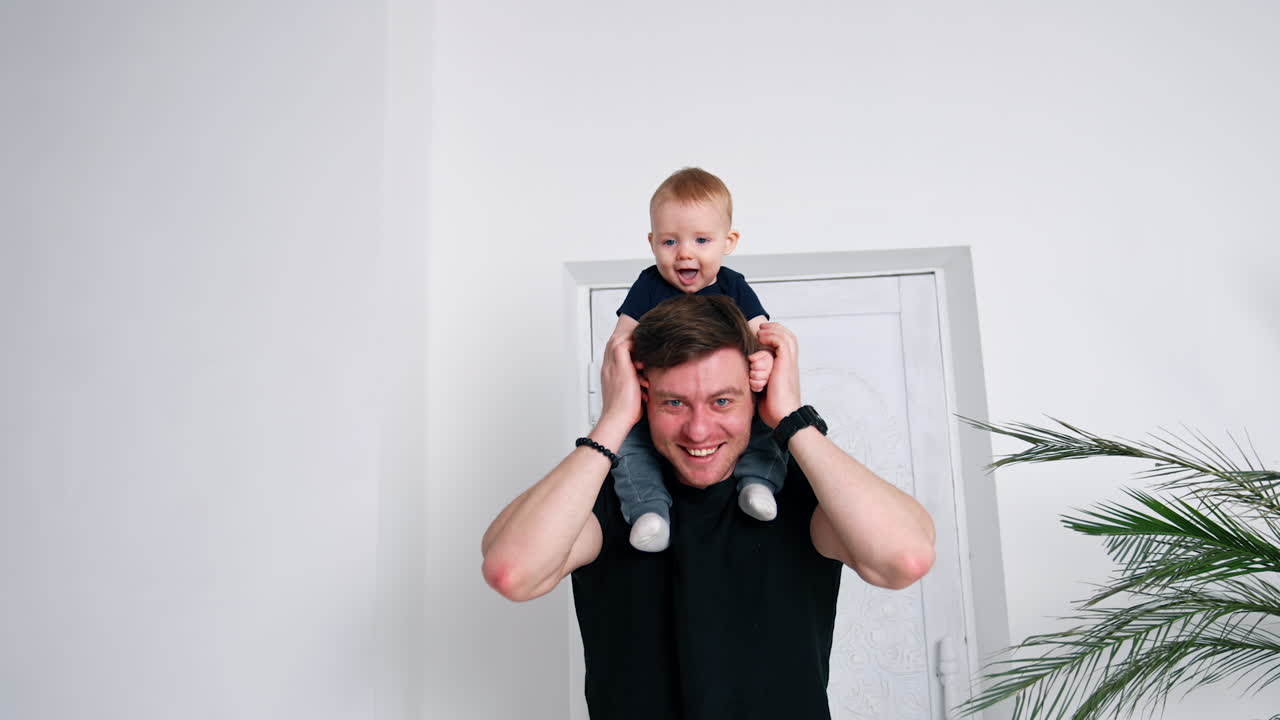 Resilient Caucasian man in black t-shirt holding a baby on his shoulders. Happy father and son portrait.