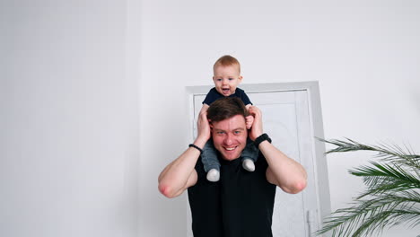resilient caucasian man in black t-shirt holding a baby on his shoulders. happy father and son portrait.