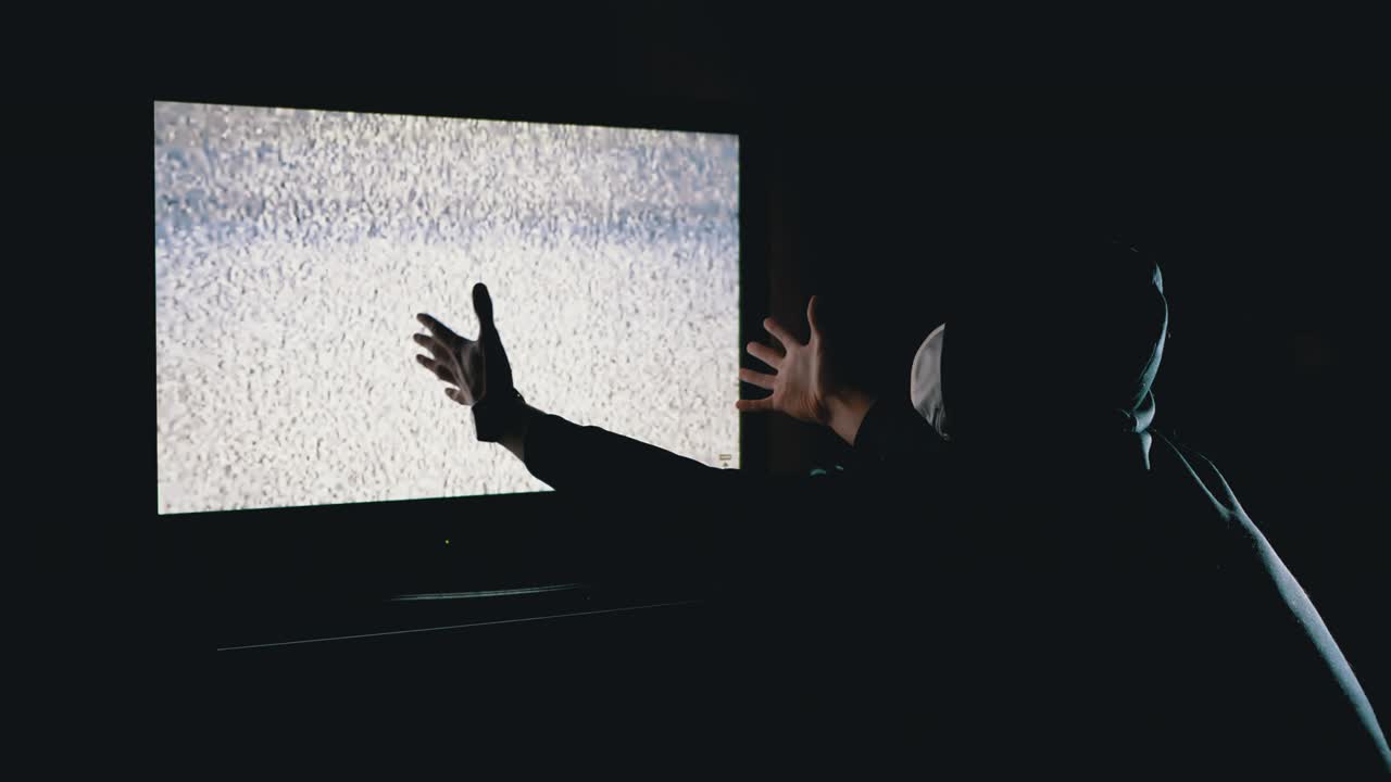 휴드와 의료 마스크를 입은 실루 남자가 손을 들고 tv 간섭을 보고 있습니다.