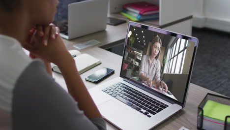 sección media de una mujer afroamericana haciendo una videollamada en una computadora portátil con una colega en la oficina