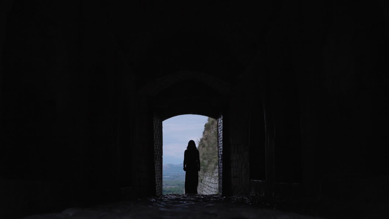 Woman's silhouette in a dark stone archway of Rozafa Castle Albania, slow motion