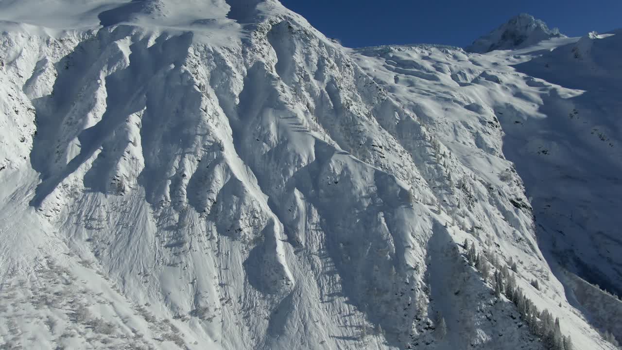 눈 인 산꼭대기 위의 드론 비행, 골짜기, 나무, 그리고 그림자 패턴, 은 파란 하늘