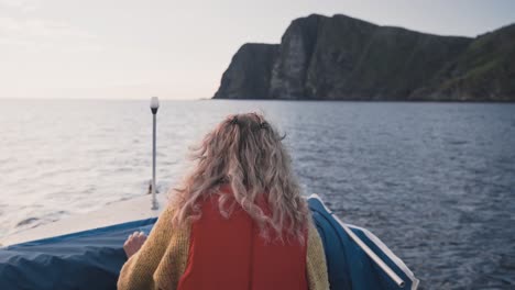 attractive blonde female boating near runde island coastline, back view