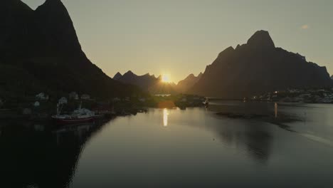 Sunlight-reflects-of-fjord-water-near-coastal-town-in-Norway,-aerial-view