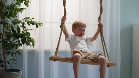 un niño pequeño sonriente se sienta en un columpio suspendido en la sala de estar