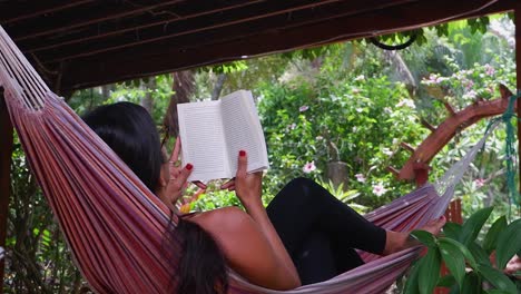 latina woman relaxes reading good book in tropical jungle hammock