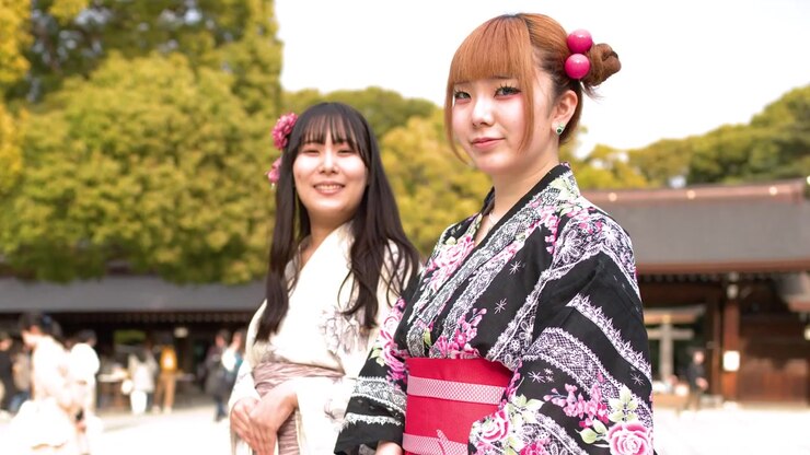 Due donne che indossano kimono floreali tradizionali si girano e sorridono nel cortile di un santuario storico giapponese.