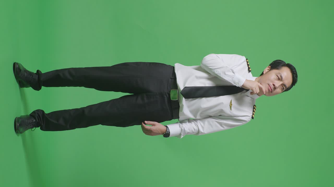 아시아 남성 조종사가 무언가에 대해 생각하고 녹색 스크린 배경 스튜디오에 서있는 동안 주위를 둘러보고 있습니다.
