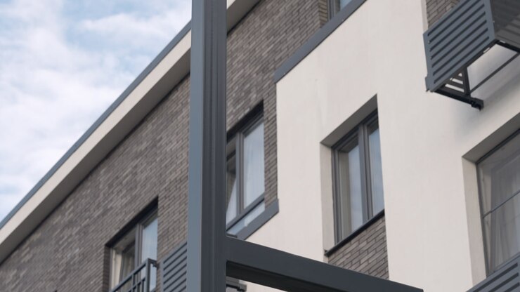 Angular LED Street Lamp Against Pale Blue Sky With Modern Building Edge, Minimalist Arm And Clean Metal Finish