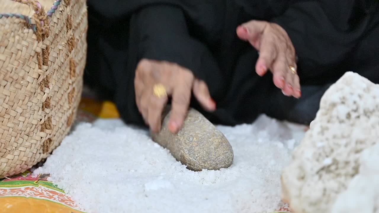 아랍 여자 가 전통적 인 방법 으로 바위 를 사용 하여 손 으로 바다 소금 을 분해 하고 있다