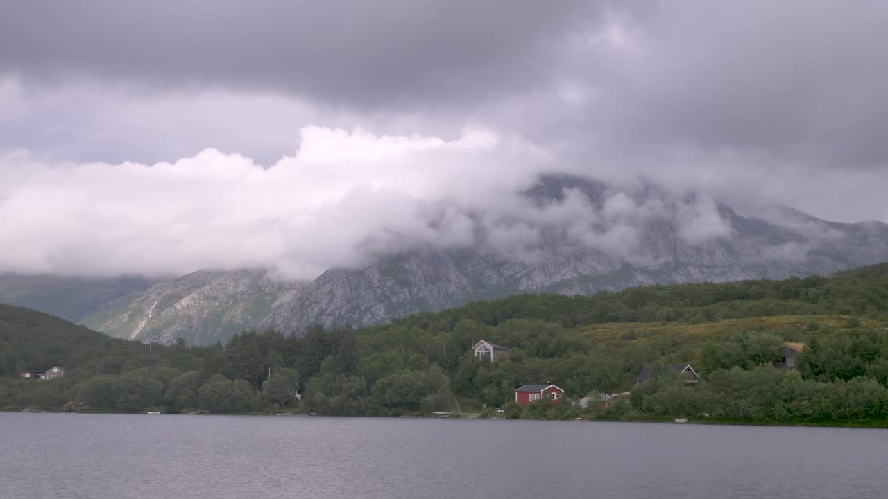 ノルウェーの湖の前に小屋があり、山肌を流れる雲
