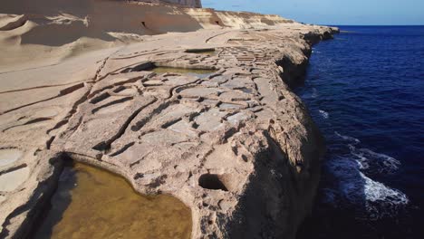 low drone tilt reveal of gozo salt pans on clear sunny day, malta