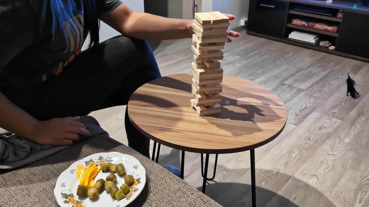 Persona che rimuove con attenzione un blocco di legno da una torre Jenga durante una rilassante serata a casa