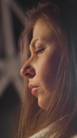 young woman with brunette hair immersed in thoughts sits alone in semi-dark living room. thoughtful female looks away and contemplates serious problems