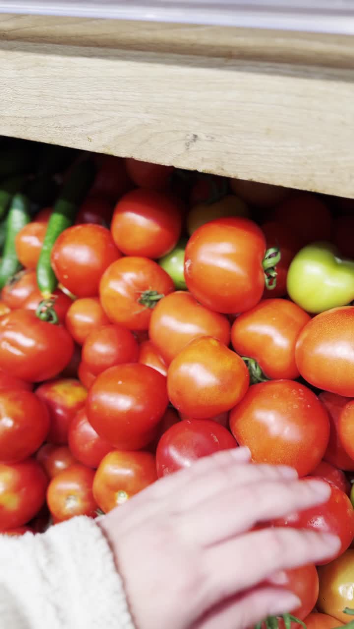 Person selecting a tomato in a grocery store