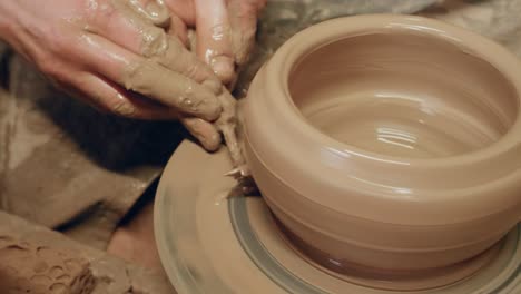 apprentice scraping off excess clay with triangle knife on ancient revolving pottery wheel