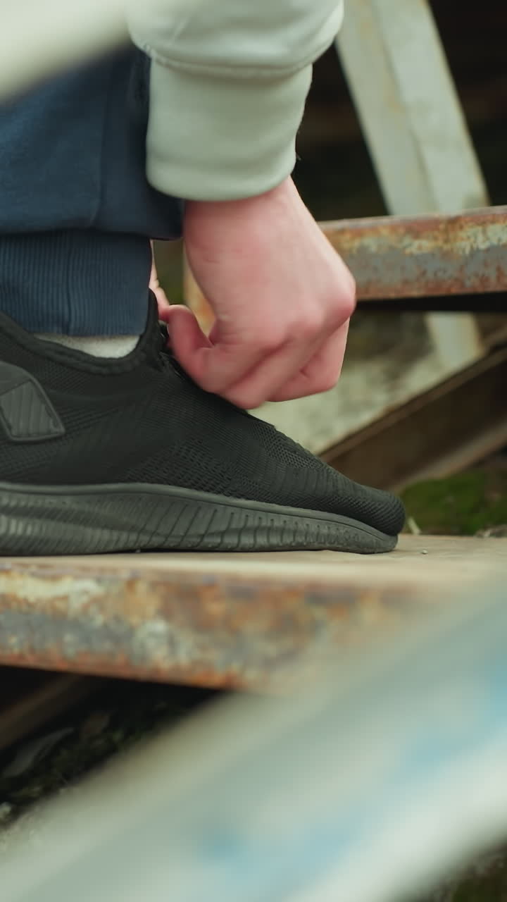 Close-up of a person bent down adjusting his shoelace while standing on a rusty staircase