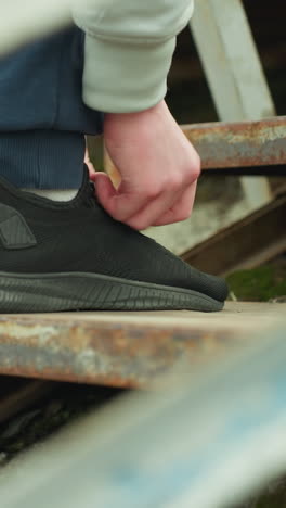 close-up of a person bent down adjusting his shoelace while standing on a rusty staircase