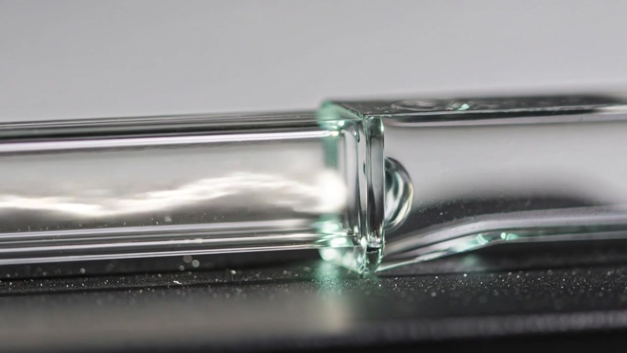 Un front lumineux en mouvement provenant d'une perturbation interne se réfracte au raccord du tube sur une paillasse de laboratoire.