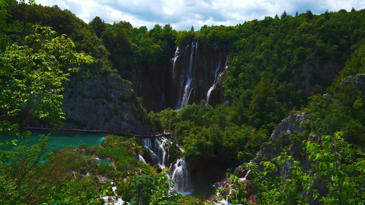 Waterfall flowing into turquoise lakes surrounded by lush forest in Plitvica National Park, Croatia