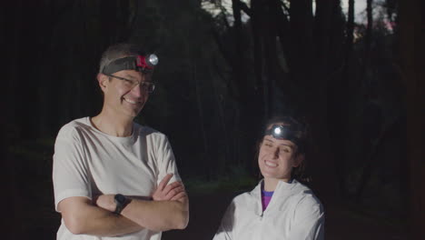 happy athletes with headlights in forest at night