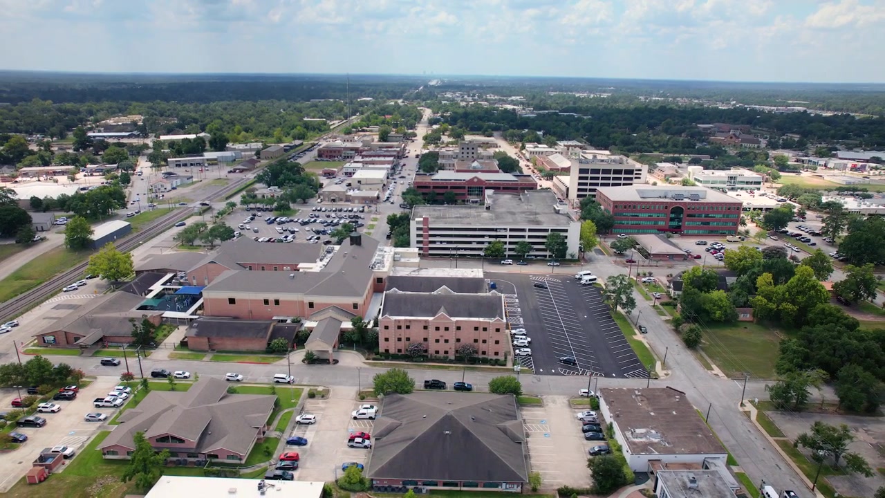 Riprese Aeree con Drone che Orbitano da Sinistra a Destra sopra il Centro di Conroe, Texas, Mostrando il Tribunale della Contea di Montgomery, gli Edifici del Centro, le Strade e il Paesaggio Urbano Circostante sotto un Cielo Luminoso Parzialmente Nuvoloso