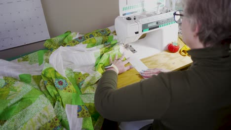 over the shoulder view of a senior woman sewing the border on assembled quilt blocks to complete the pattern