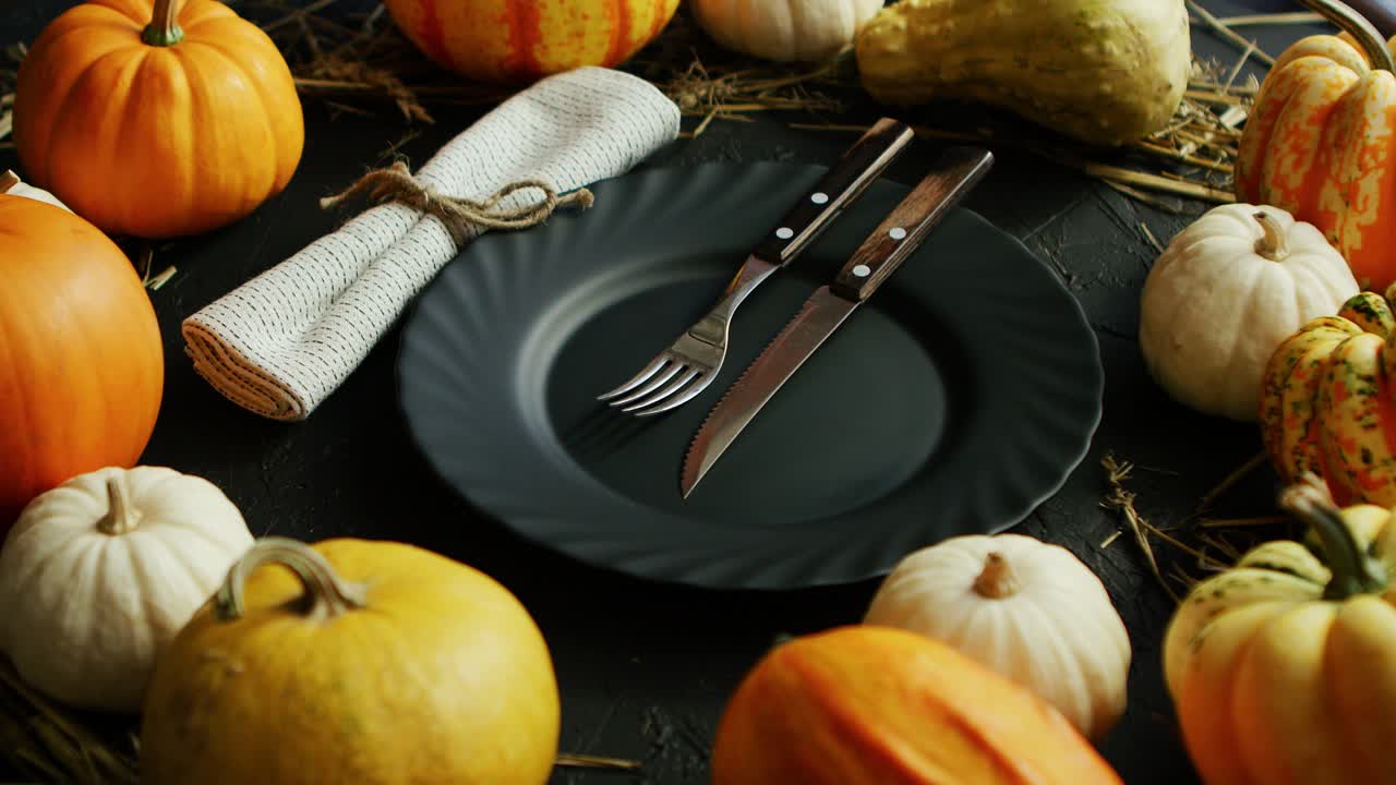plato negro y cubiertos rodeados de calabazas