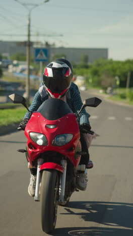 dos hermanas viajan en una bicicleta eléctrica roja mientras viajan por una carretera urbana, el fondo presenta una vista borrosa de automóviles, edificios y postes eléctricos, con una visión borrosa de un coche saliendo de una curva