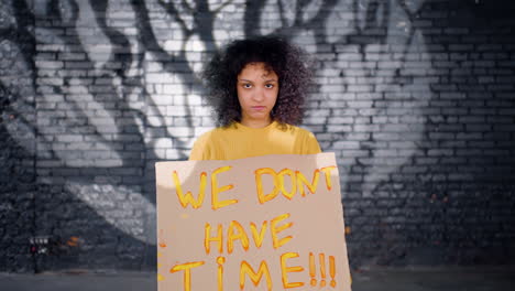 joven activista medioambiental serio sosteniendo un cartón con la inscripción "no tenemos tiempo" y mirando la cámara