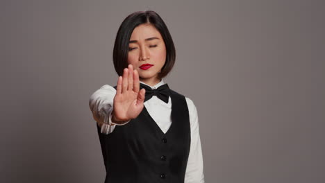 asian administrator showing stop sign with palm raised in studio,