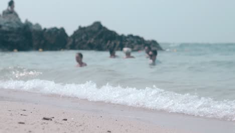 Weiße-Schäumende-Wellen-Rollen-Am-Sandstrand-Gegen-Verschwommene-Menschen