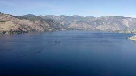 Drone-flying-over-houses-towards-lake-and-mountains