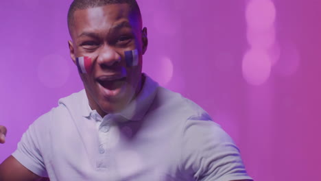 Animation-of-glowing-lights-over-african-american-man-with-flag-of-france-on-face-cheering