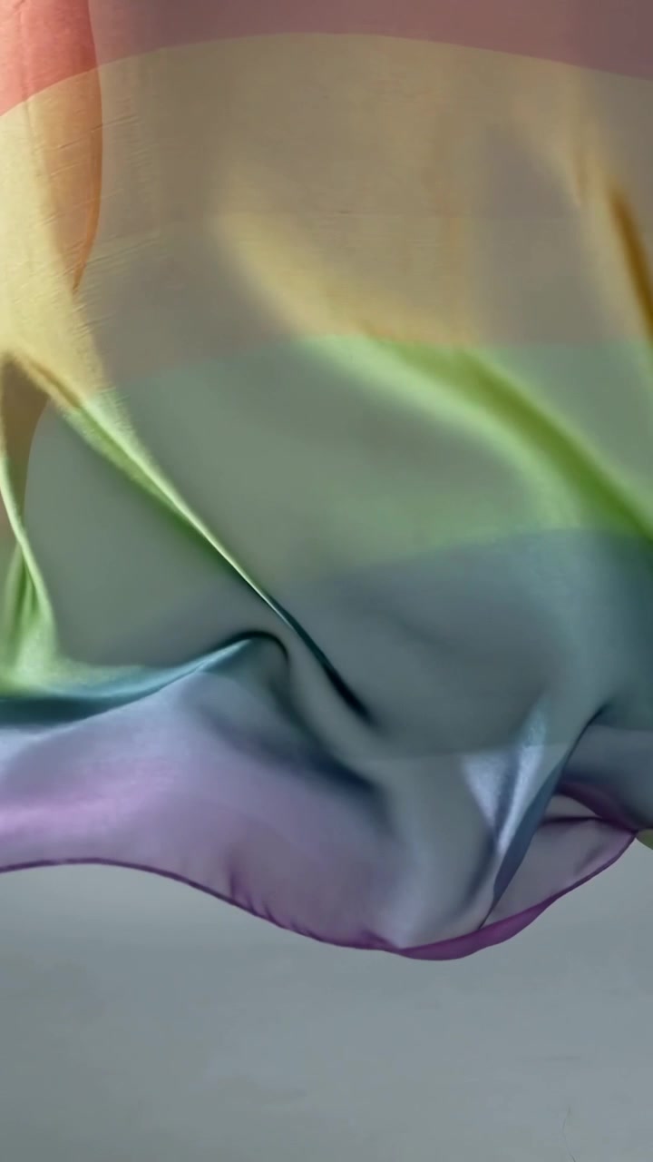 Video vertical: Bandas de satén pastel con los colores del arcoíris ondeando en un estudio, moviéndose con la brisa y mostrando su brillo.