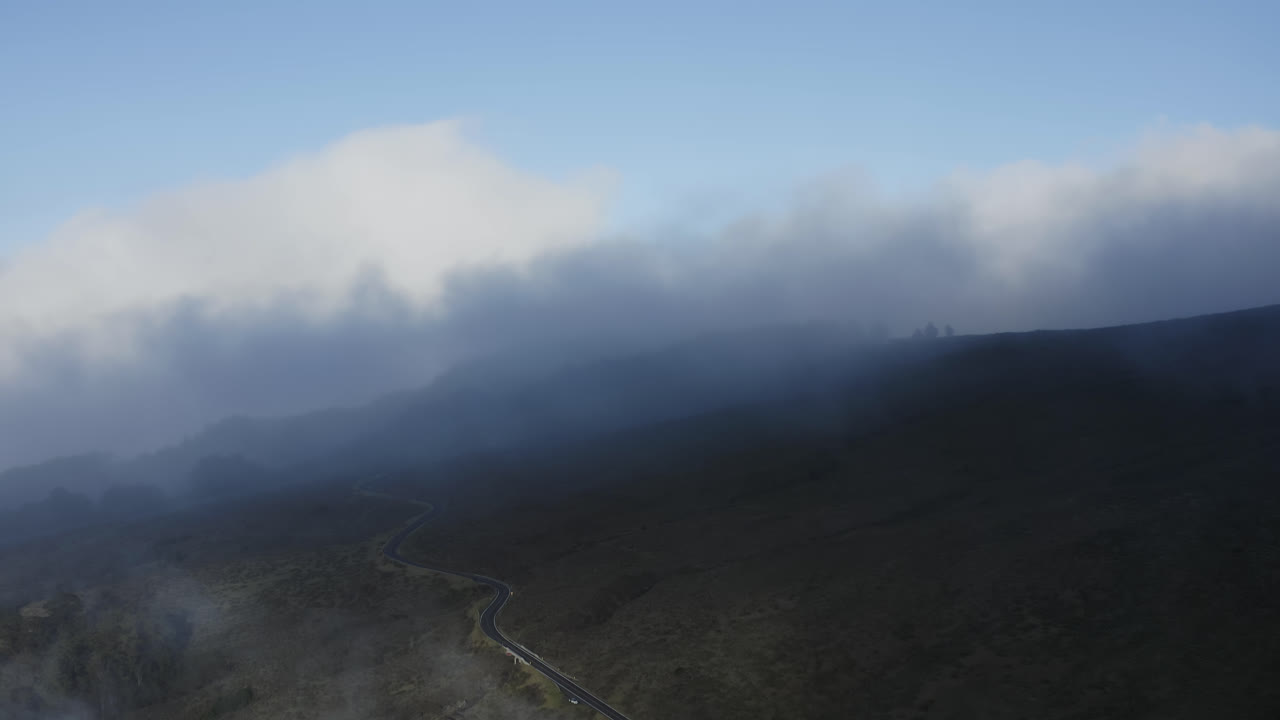 las nubes del estrato fluyen suavemente por las laderas de haleakala por encima de la sinuosa carretera en maui.