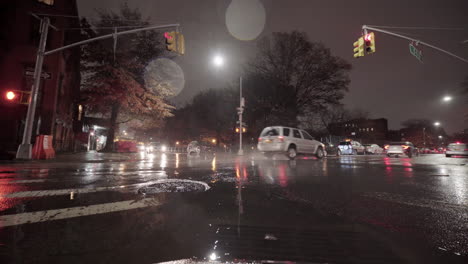 Coche-Atravesando-Un-Charco-De-Lluvia-En-La-Ciudad-Por-La-Noche-Y-Coche-Con-Luz-Roja