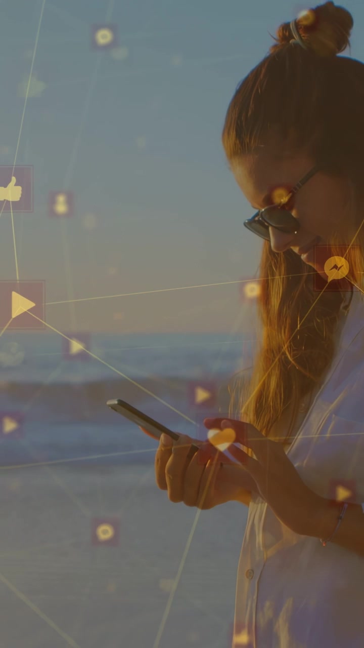 Video verticale: Donna che tocca il telefono al tramonto in spiaggia, controlla gli avvisi e disegna icone dei social media.