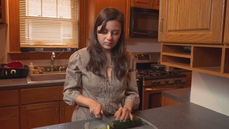 mujer asiática de raza mixta cortando pepinos en la tabla de cortar, preparando una comida saludable