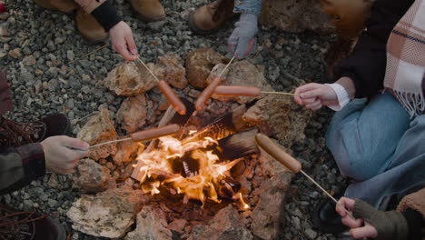 top view of hands of a group of teenage friends roasting sausages on the bonfire