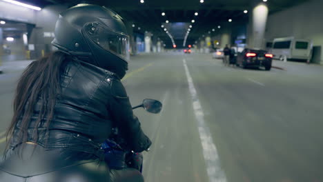 a woman rides a motorcycle past the camera on an empty street in los angeles, ca