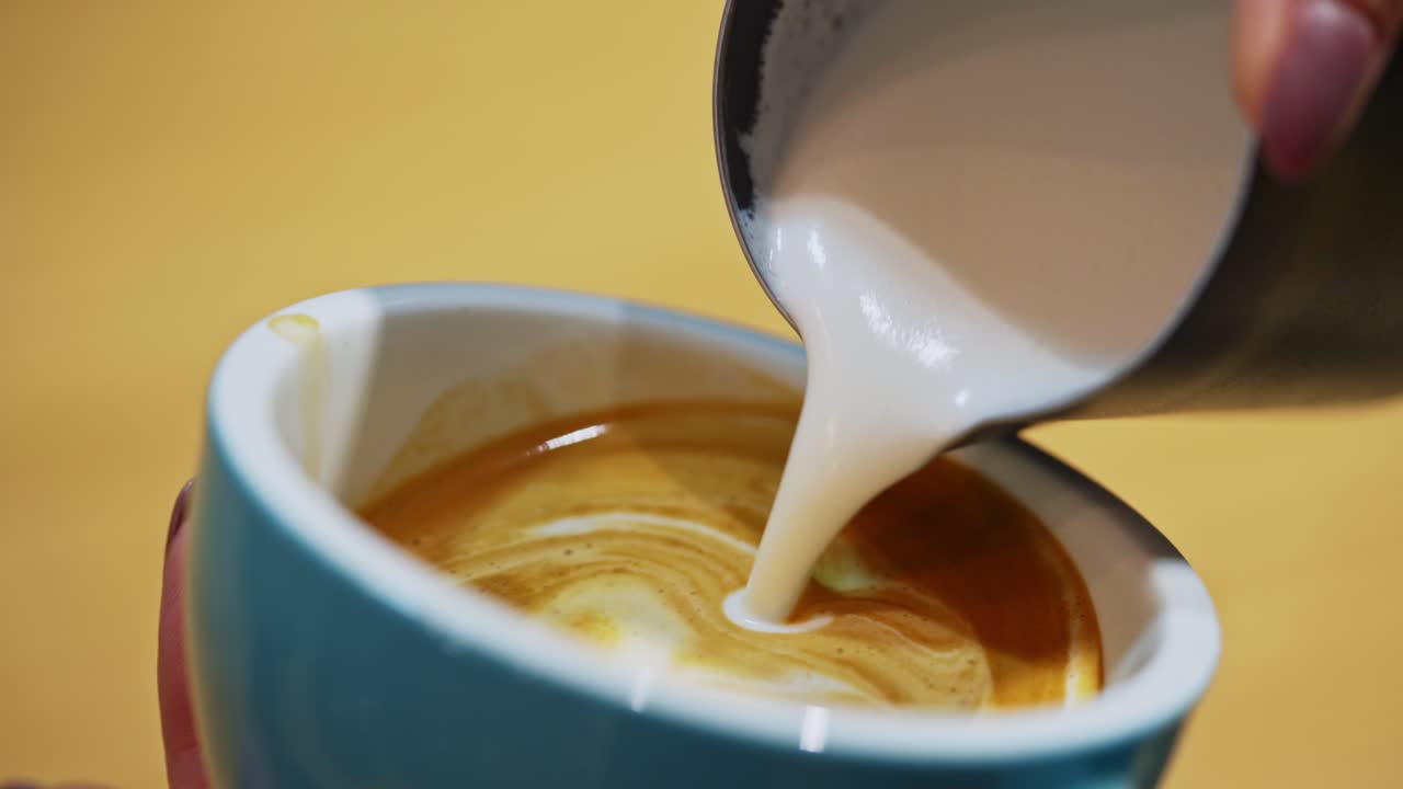 Barista making of cafe latte art. Heart shape on coffee in a cup. Making latte by pouring milk slowly into a blue cup. Close-up.