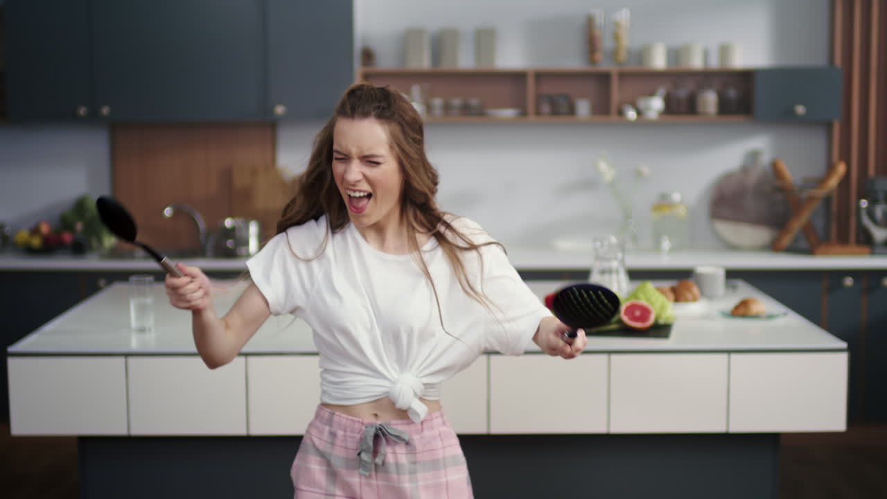 Donna appassionata che suona la batteria virtuale con cucchiai con la cucina sullo sfondo.
