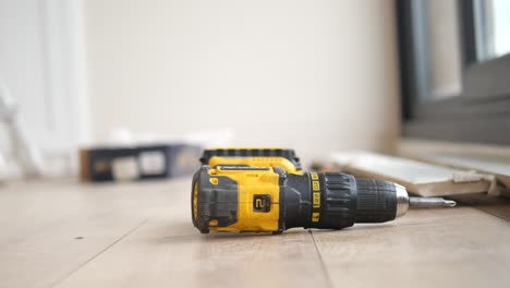 a yellow and black cordless drill lying on a wooden floor, in front of a window