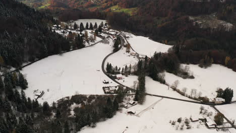 Aerial-of-small-village-in-winter-overlooking-a-green-valley