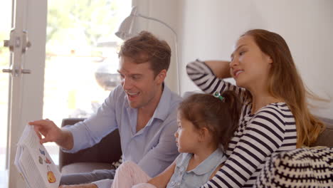 Padres-Leyendo-Con-Su-Hija-En-El-Sofá-En-Casa