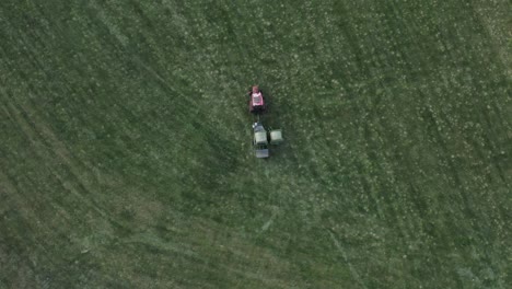 tractor with wrapping machine drives on field with fresh green hay bale, aerial